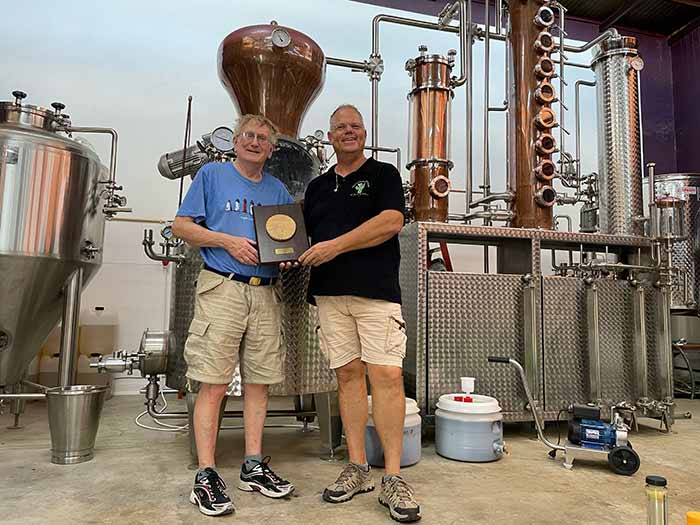Eric Gietman, Master Distiller at The Cadushy Distillery receiving a plaque from Professor George Buckley of Harvard University, featuring a piece of the mast from Captain Don's sailboat, the Valerie Queen.